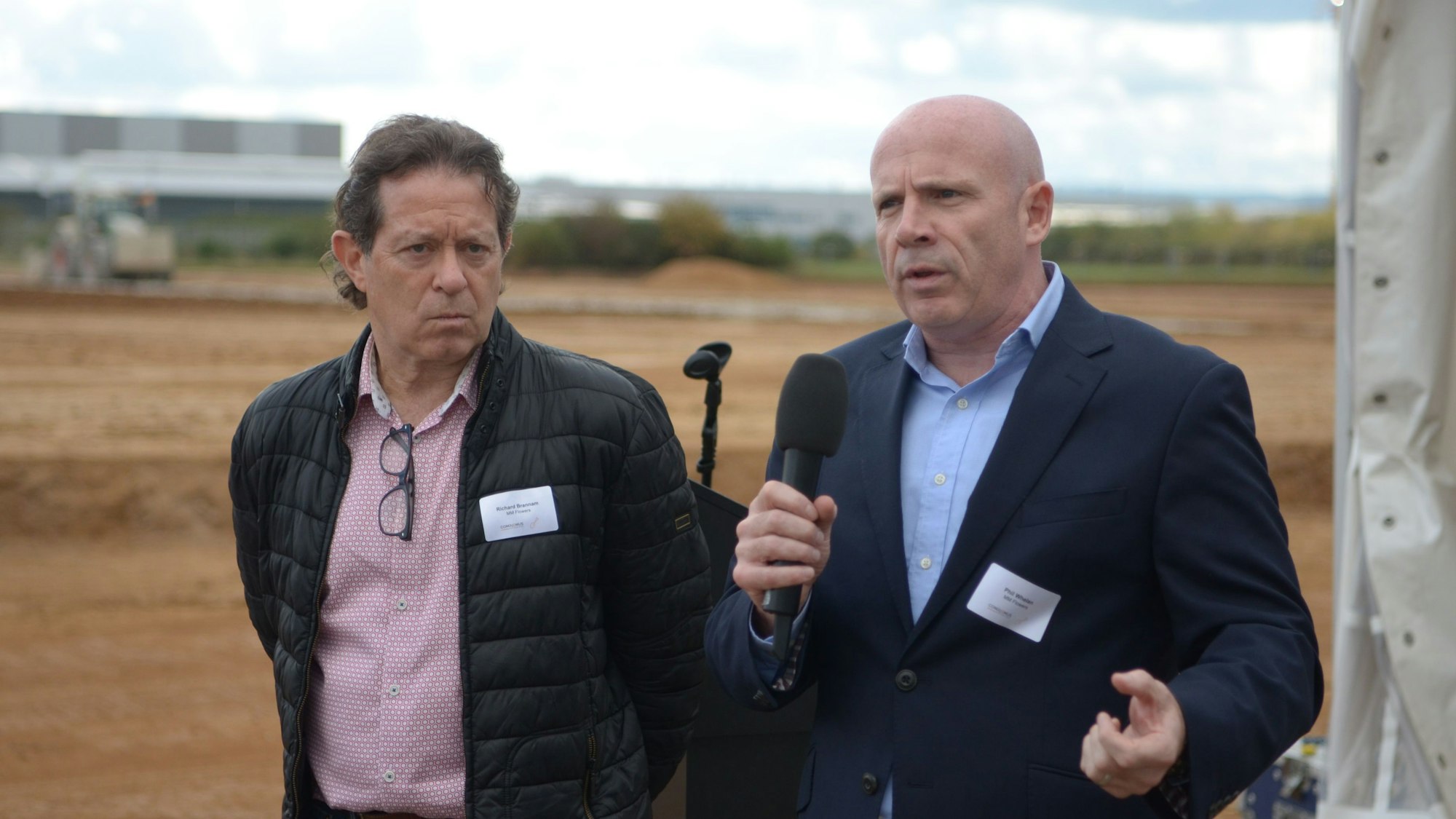 Zwei Männer stehen nebeneinander, einer spricht in ein Mikrofon.