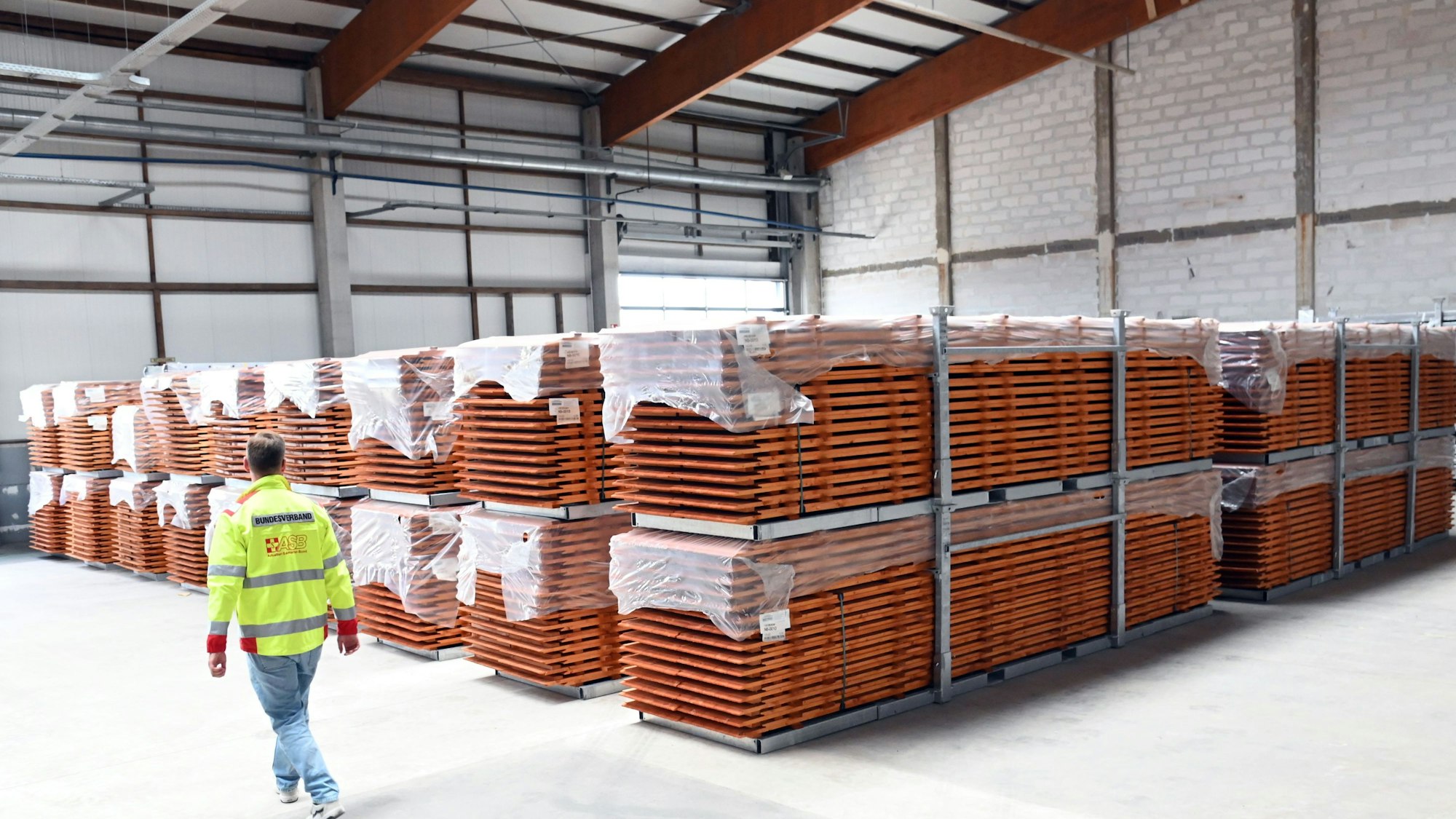 Ein Mann in neongelber Jacke läuft an Stapeln mit Tischen und Bänken vorbei. Sie sind typisch orange. Foto: Alexander Schwaiger