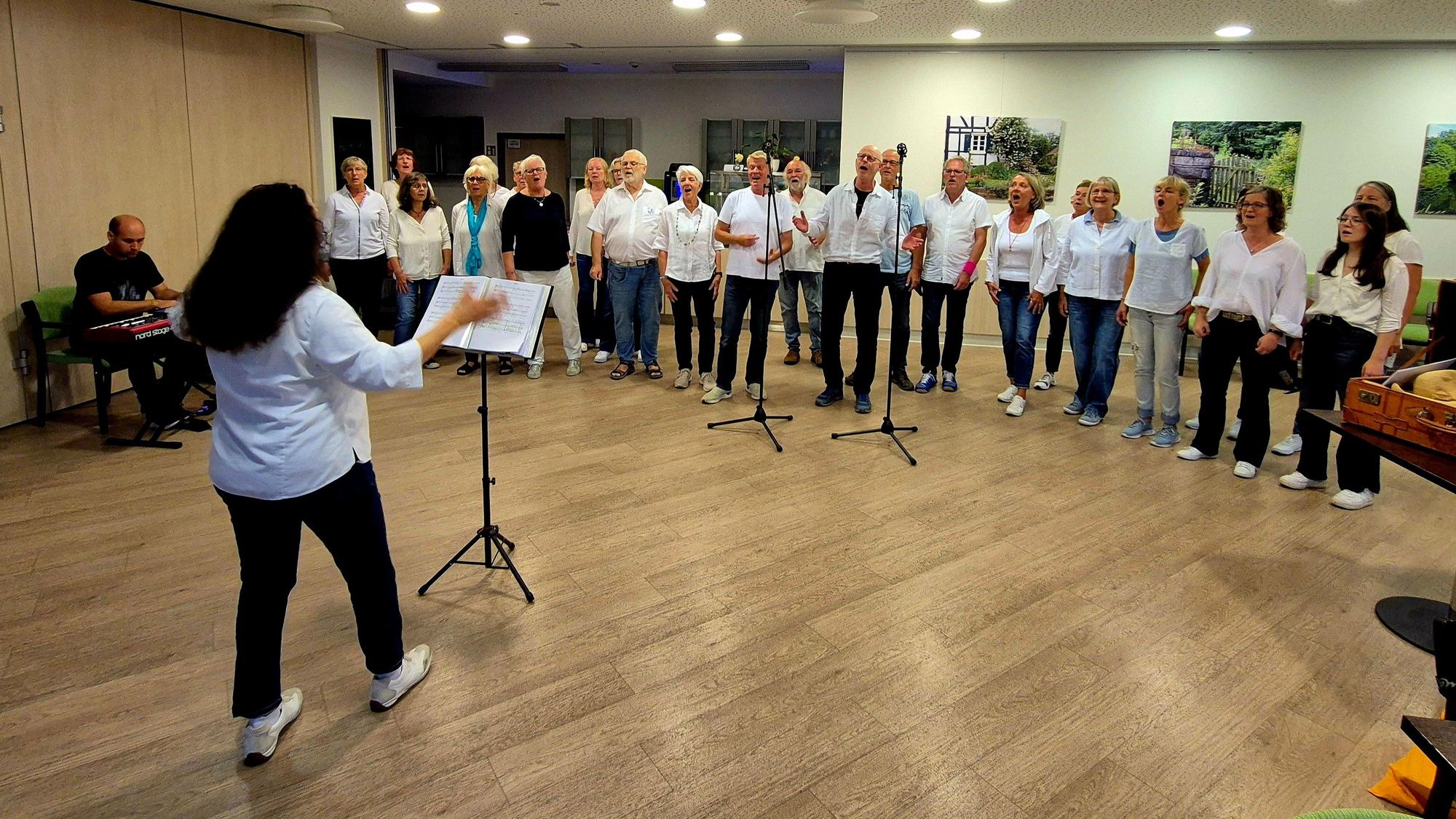 Eine Frau dirigiert einen Chor, der im Halbkreis um sie herum steht.