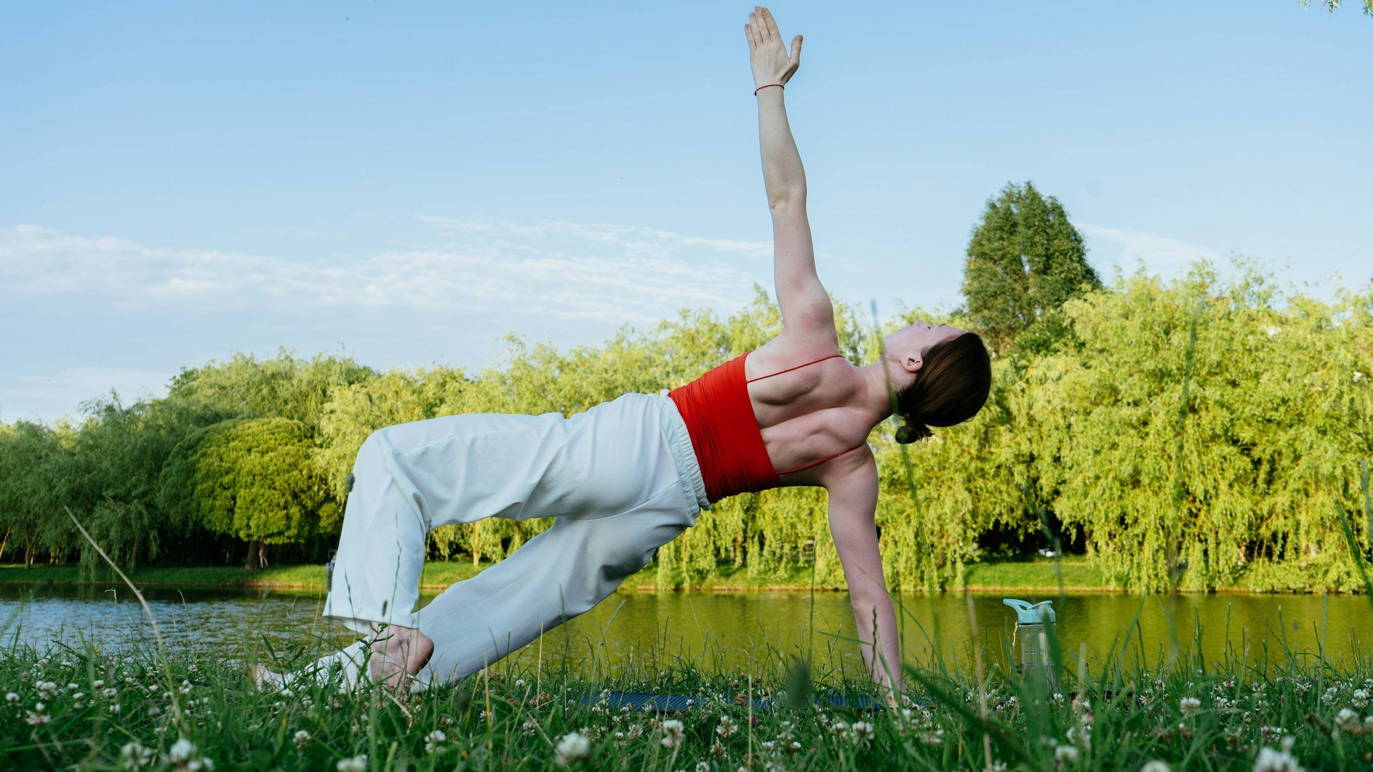Woman practicing yoga outdoors on grass by water for relaxation model released, Symbolfoto, KANF00063