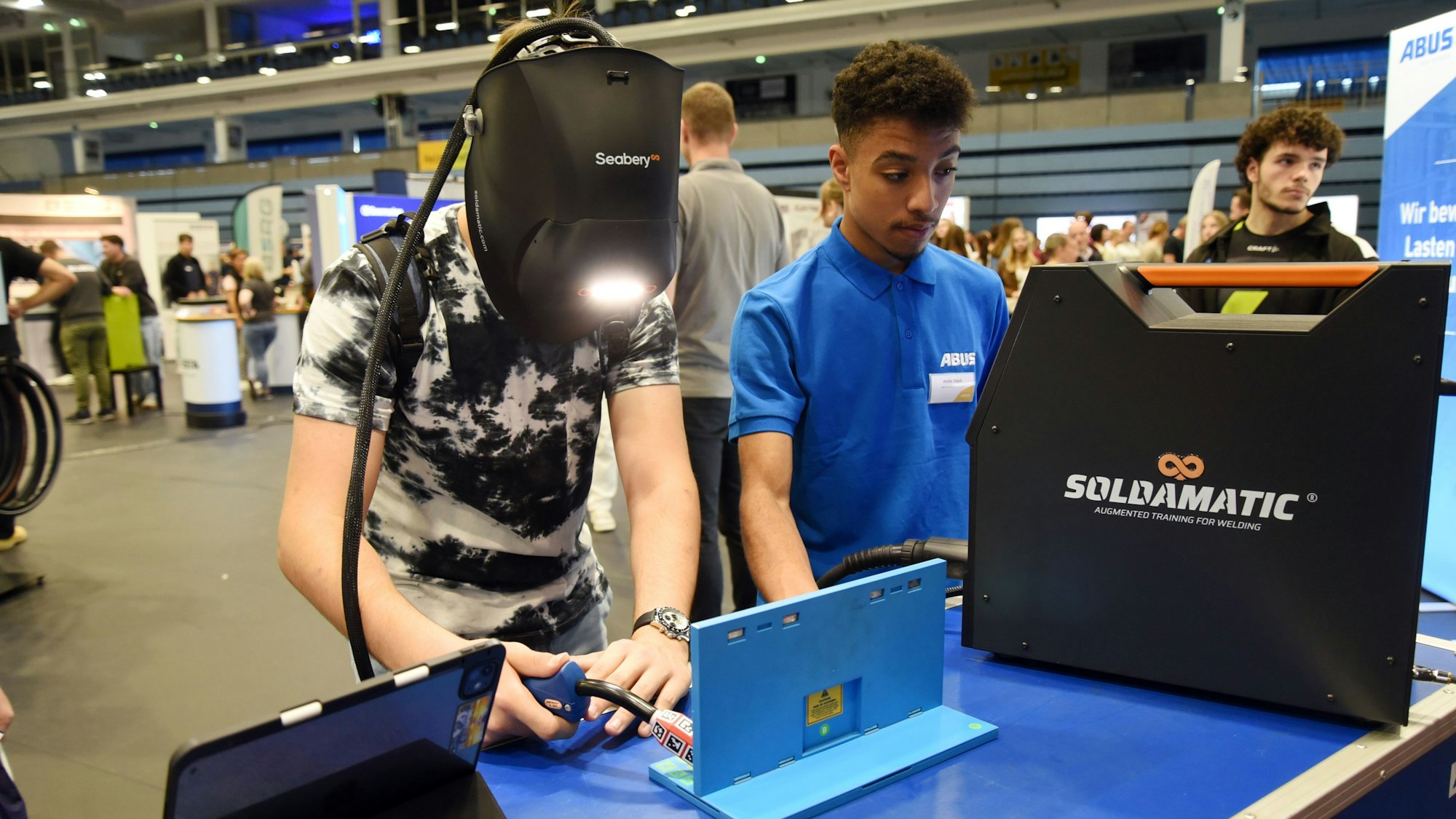 Ein junger Mann mit Schweißerhaube hantiert mit einem technischen Gerät.