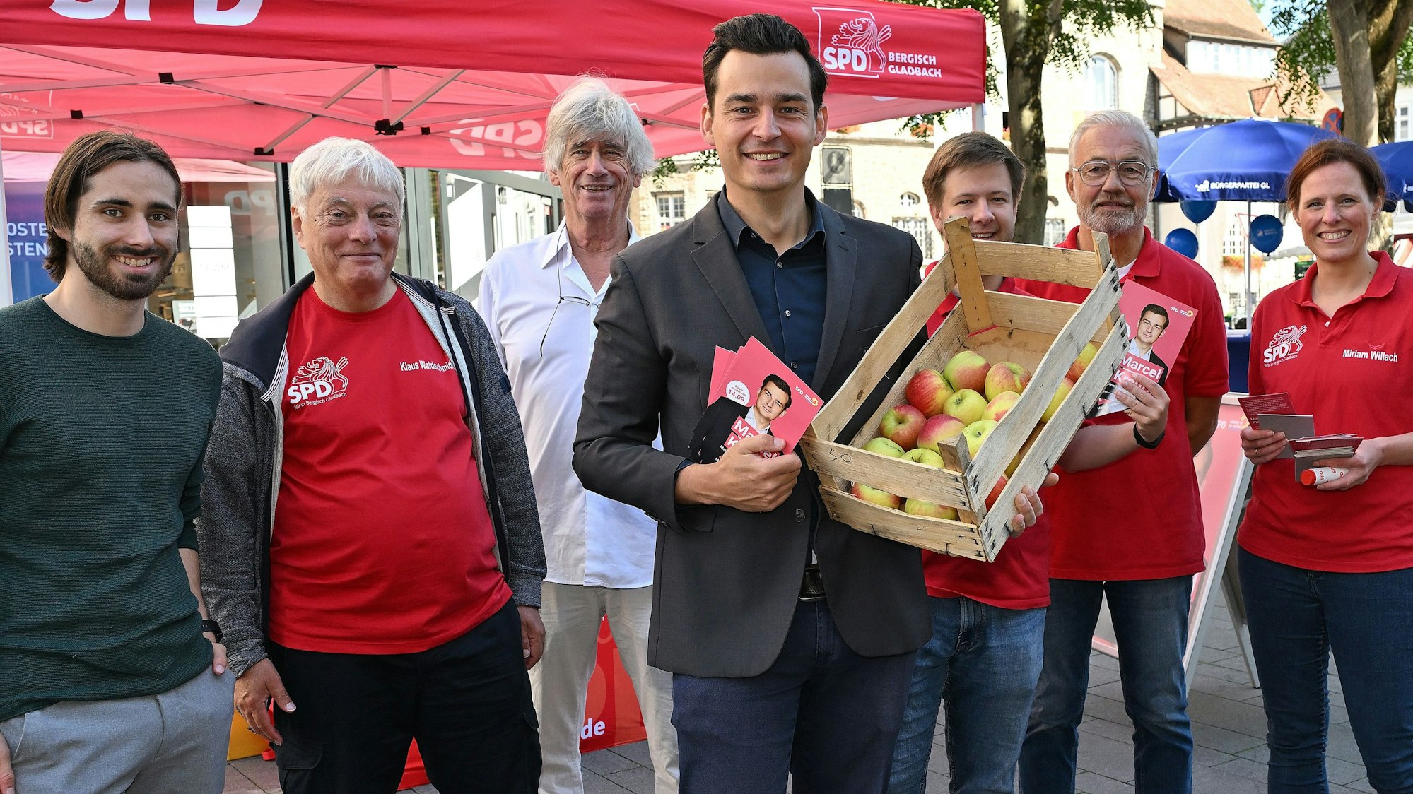 SPD-Bürgermeisterkandidat Marcel Kreutz hält eine hölzerne Kiste voller Äpfel im Arm.