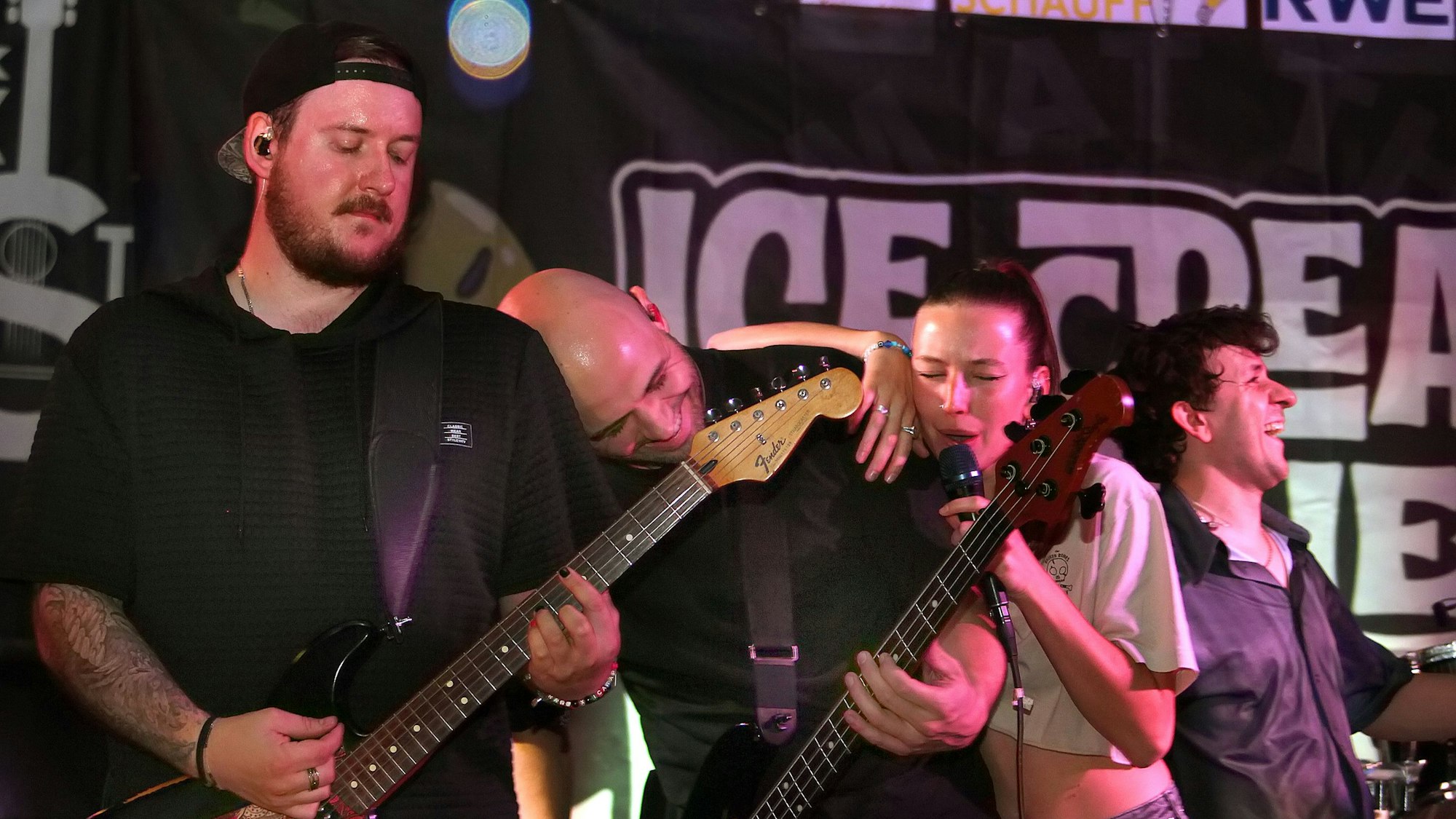 Das Bild zeigt die Band, der Bassist hat den Kopf auf der Schulter des Gitarristen geschmiegt, die Sängerin lehnt sich wiederum an den Bassisten an.