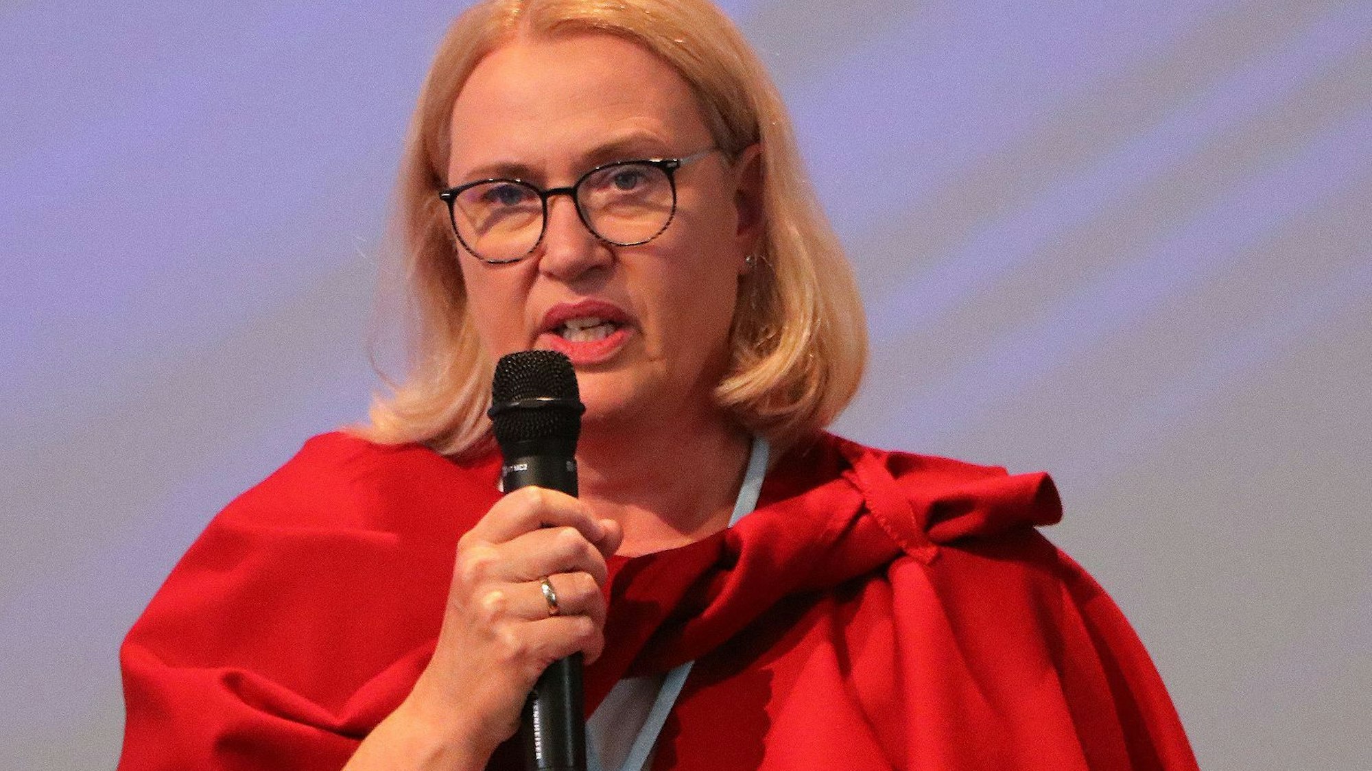 Auf dem Bild ist das Portrait einer Frau zu sehen, sie hält ein Mikrofon in der Hand.