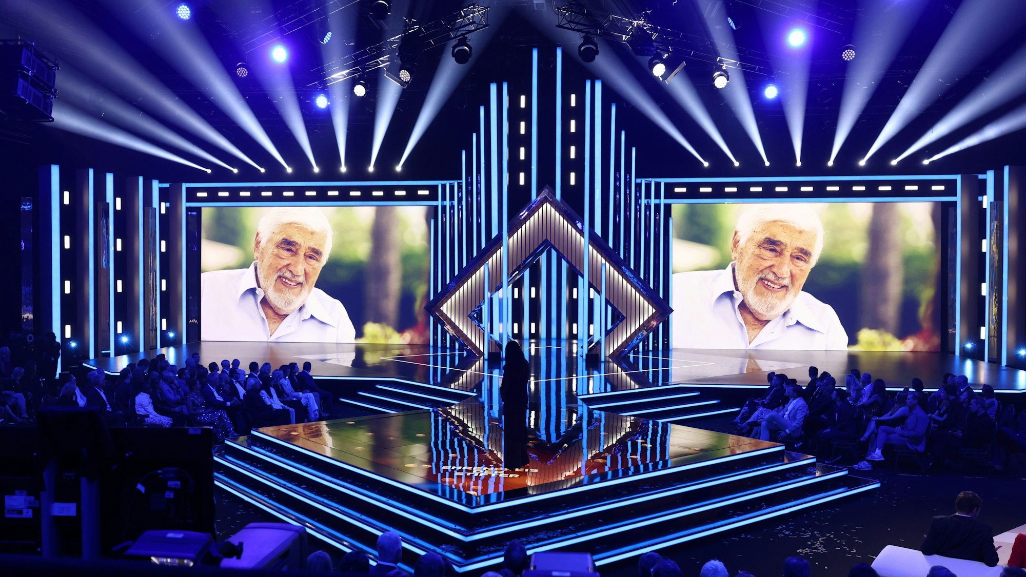 25.09.2024, Nordrhein-Westfalen, Köln: Fotos von Mario Adorf sind bei der Verleihung des Deutschen Fernsehpreises 2024 im Coloneum bei dem Ehrenpreis der Stifter eingeblendet, während Schauspielerin Iris Berben auf der Bühne steht. Der Deutsche Fernsehpreis wird für die Programmsaison 2023/24 verliehen. Foto: Rolf Vennenbernd/dpa +++ dpa-Bildfunk +++