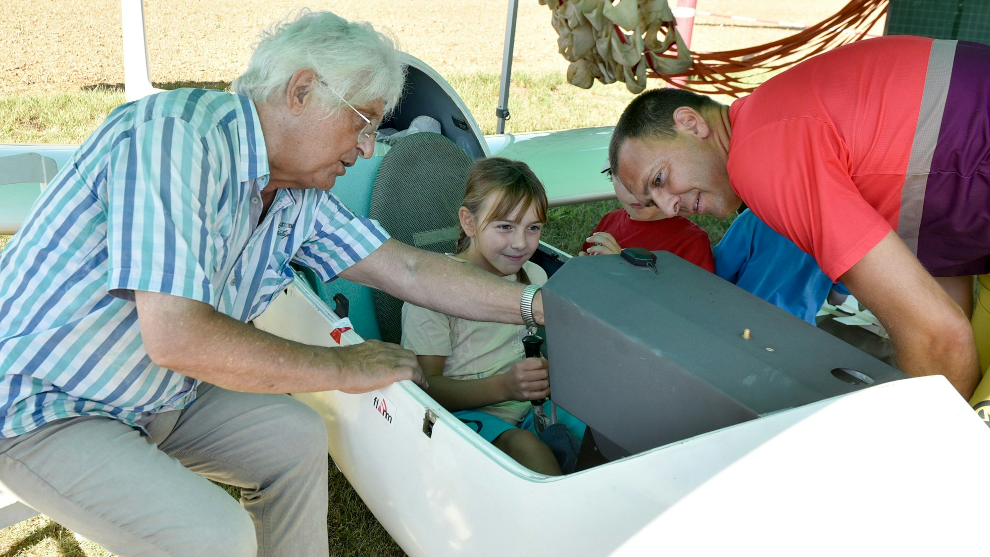 Das Bild zeigt ein junges Mädchen im offenen Cockpit. Links und rechts von ihr erklären die beiden Herren die Instrumente.