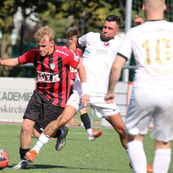 Das Bild zeigt einen Zweikampf zweier Spieler um den Ball. Weitere Akteure schauen zu.
