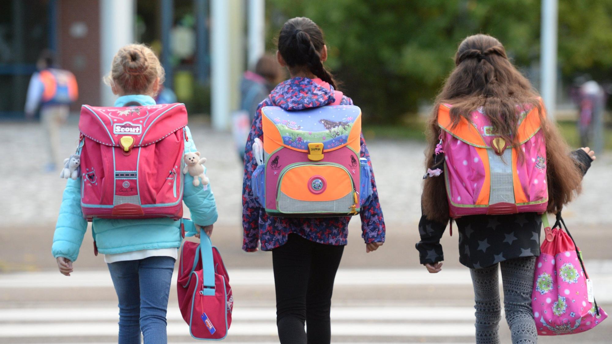 Drei Schülerinnen laufen mit ihren Schulranzen zur Schule