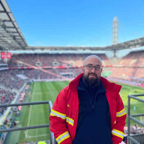 Auf dem Bild ist ein Mann in DLRG-Uniform auf der Tribüne des Rhein-Energie-Stadions zu sehen.