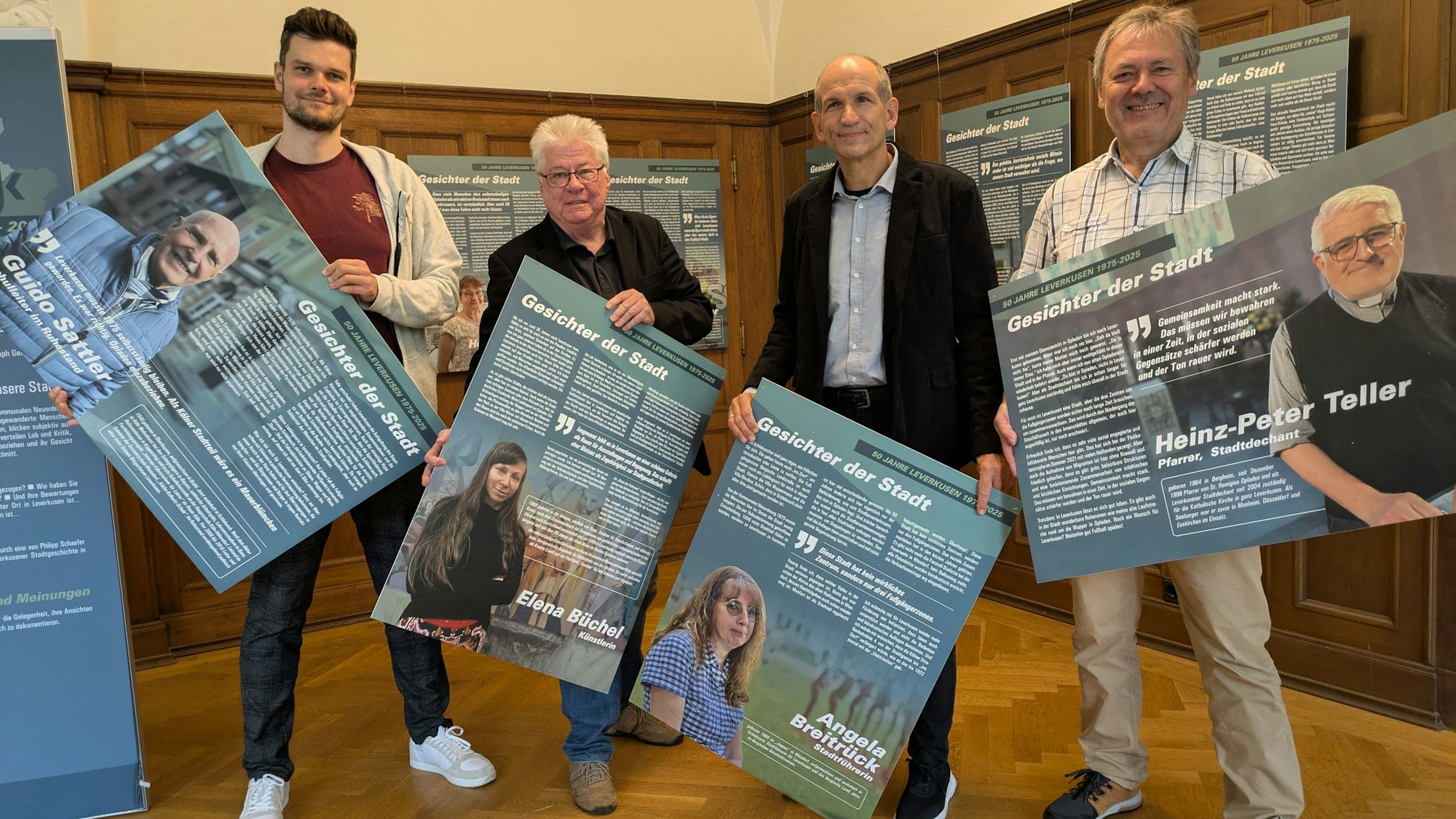 Vier Männer halten Bildtafeln in einer Ausstellung hoch.