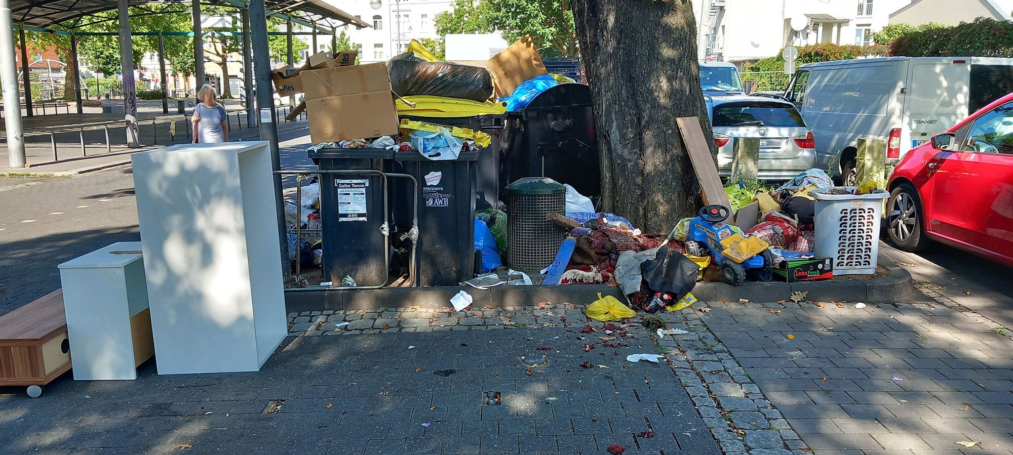 Auf einem Parkplatz stehen volle Müllcontainer und allerlei Sperrmüll neben parkenden Autos.