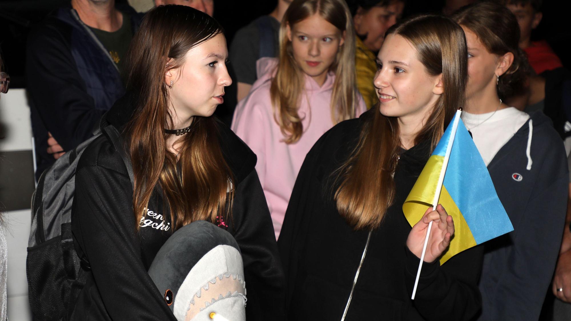 Zwei Mädchen stehen mit einer Ukrainefahne und Gepäck in der Nacht zu Montag (8. September) an der Integrierten Gesamtschule Paffrath.