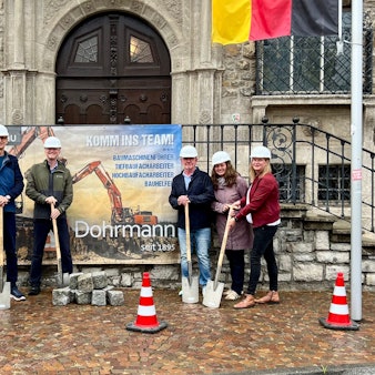 Sechs Leute, darunter der Bürgermeister, stehen mit einem Spaten in der Hand vor dem Rathaus.