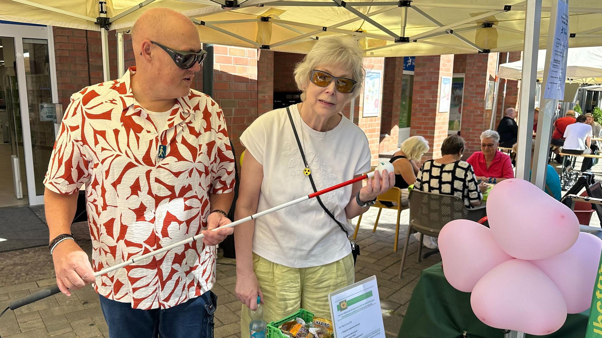 Dirk Schäfer und Gabriele Schröder am Stand der Selbsthilfegruppe für Sehbehinderte mit einem Blindenstock in den Händen.