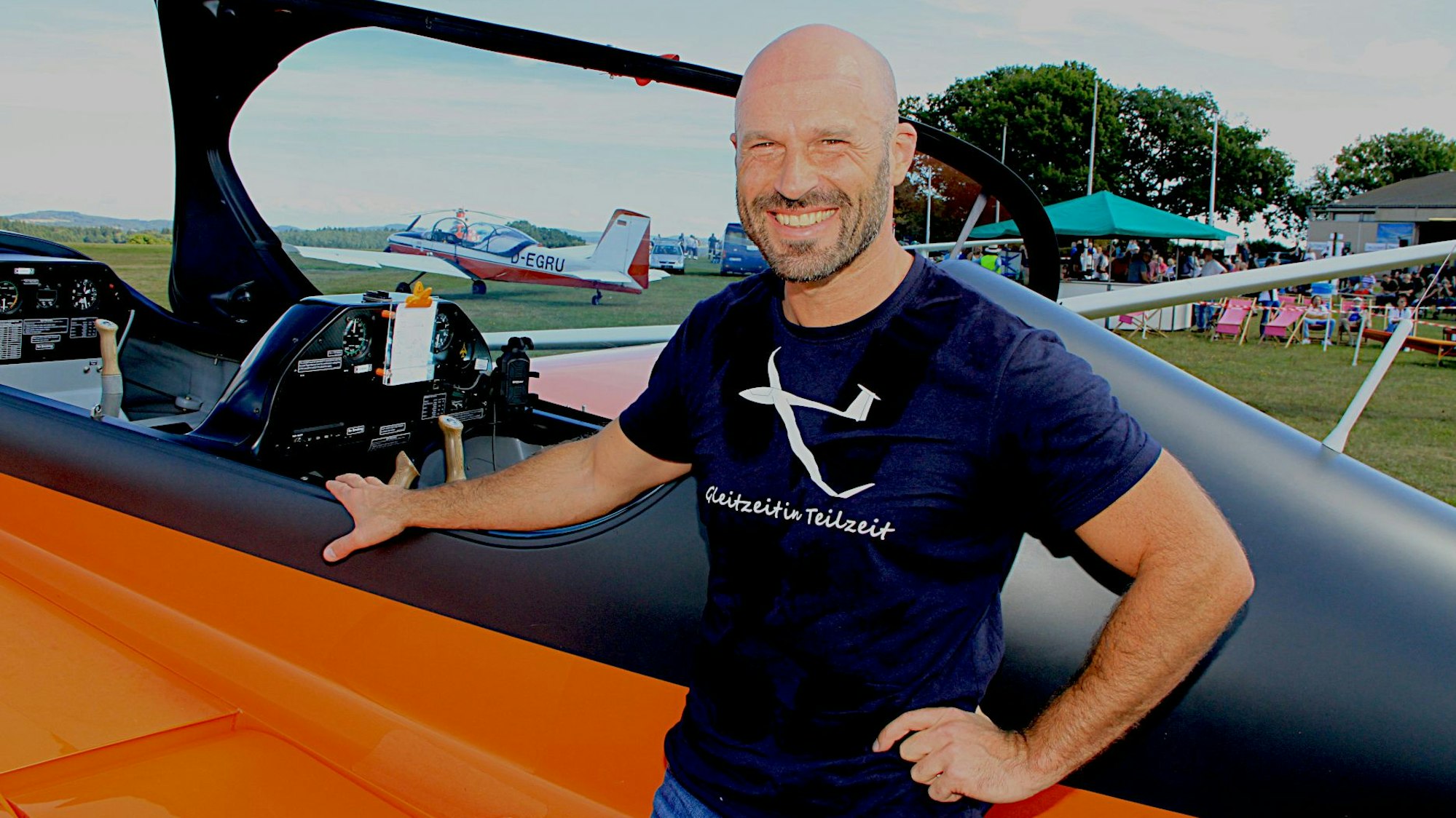 Der Pilot und Kunstflieger Robin Ermen steht vor dem geöffneten Cockpit seines Flugzeuges und lacht in die Kamera.
