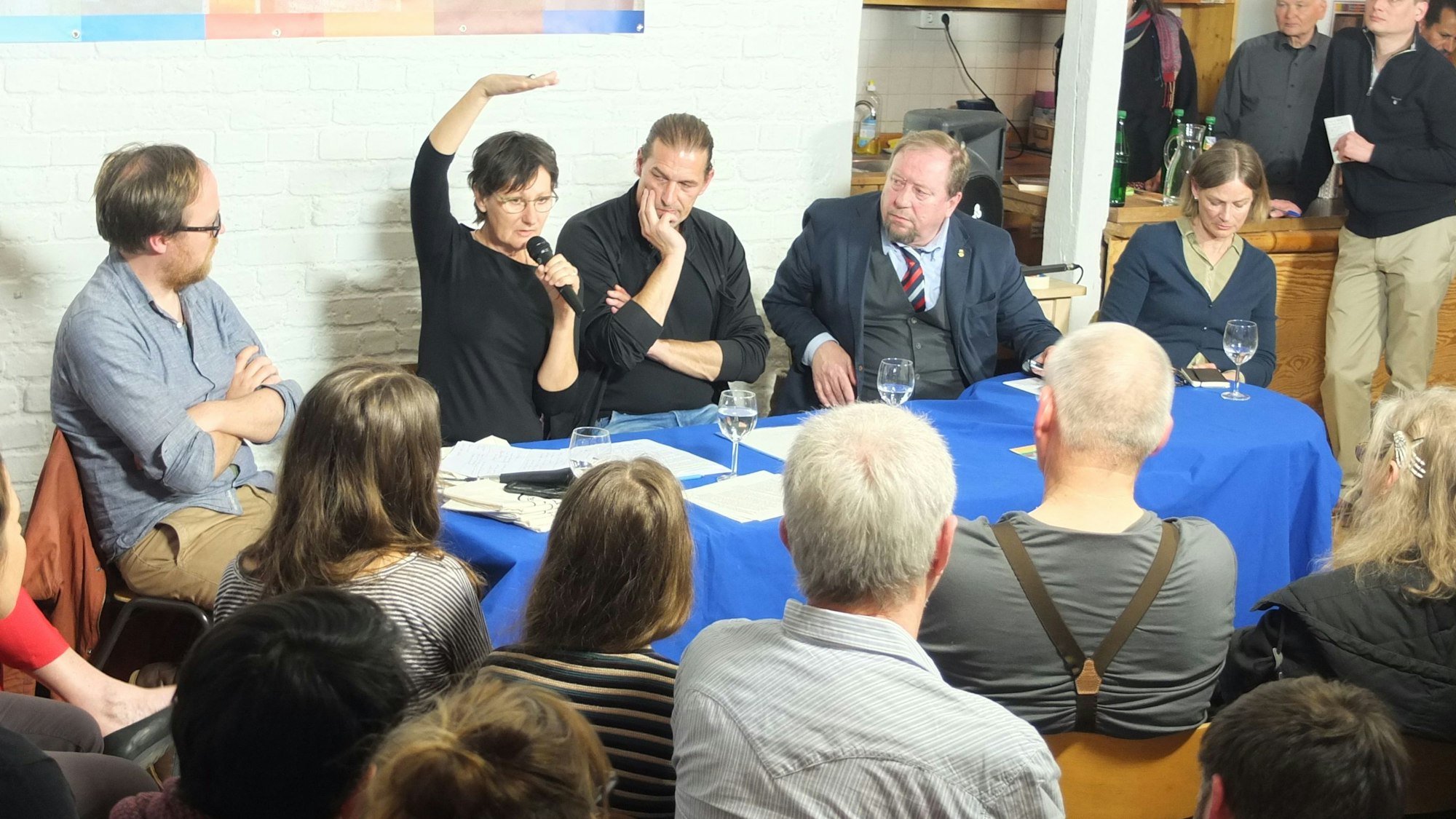 Fünf Menschen sitzen an einem Tisch, vor ihnen sitzen Zuschauer in mehreren Reihen.