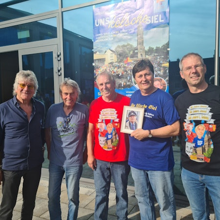 Fünf Männer stehen vor einer Glastür. Einer hält ein Bild.