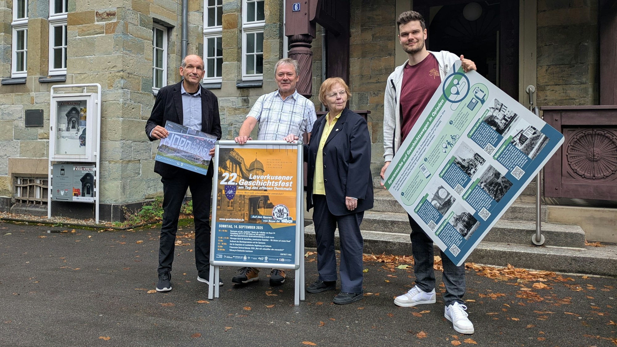 Drei Männer und eine Frau stehen mit Plakaten vor einem Gebäude.