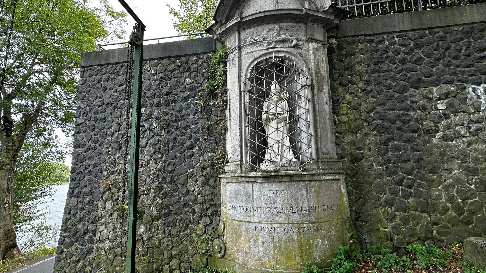 Eine Heiligenstatue aus Stein steht in einer vergitterten Nische.