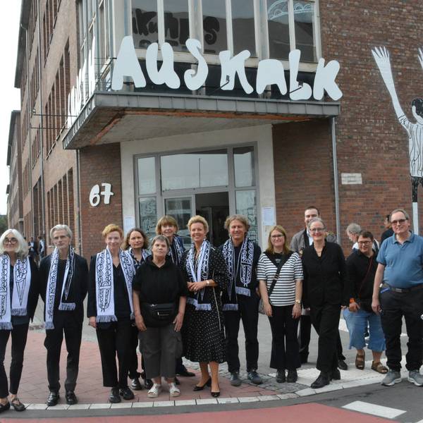 Eine Gruppe von Menschen steht vor einem Backsteingebäude mit einem Banner, auf dem Kunsthaus Kalk steht.