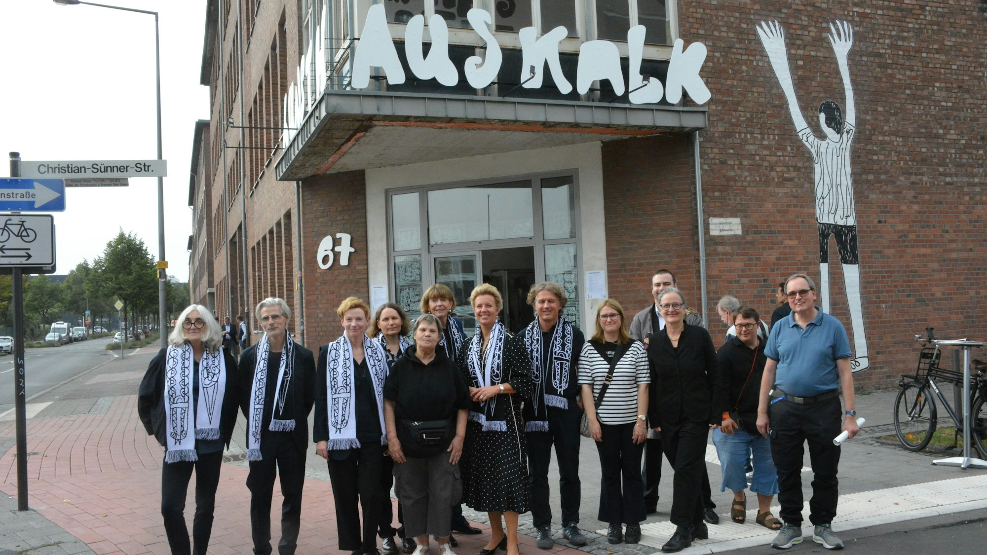 Eine Gruppe von Menschen steht vor einem Backsteingebäude mit einem Banner, auf dem Kunsthaus Kalk steht.