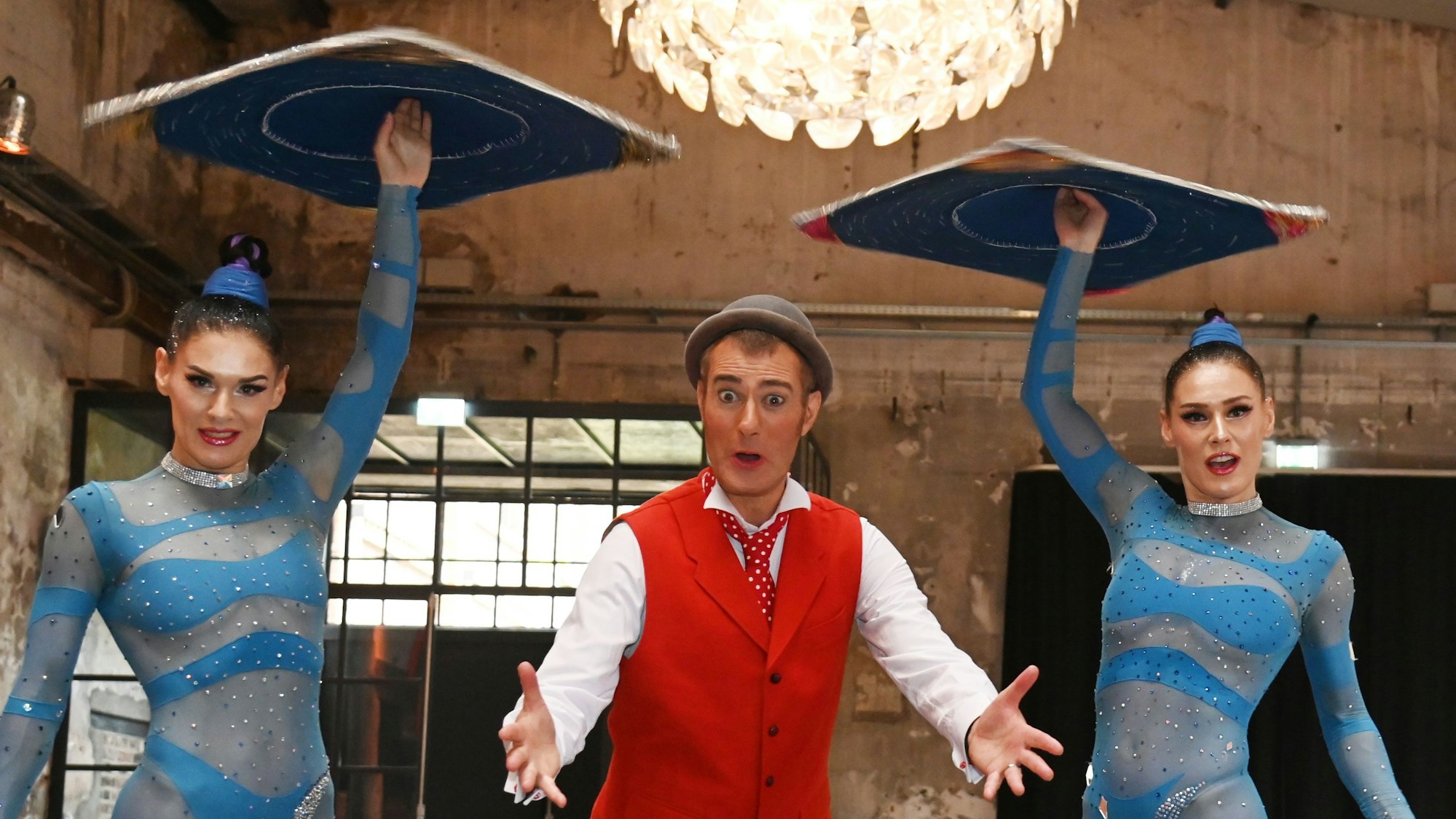 Die Crystal Sisters balancieren Scheiben, während der Clown in der Mitte in die Kamera schaut.