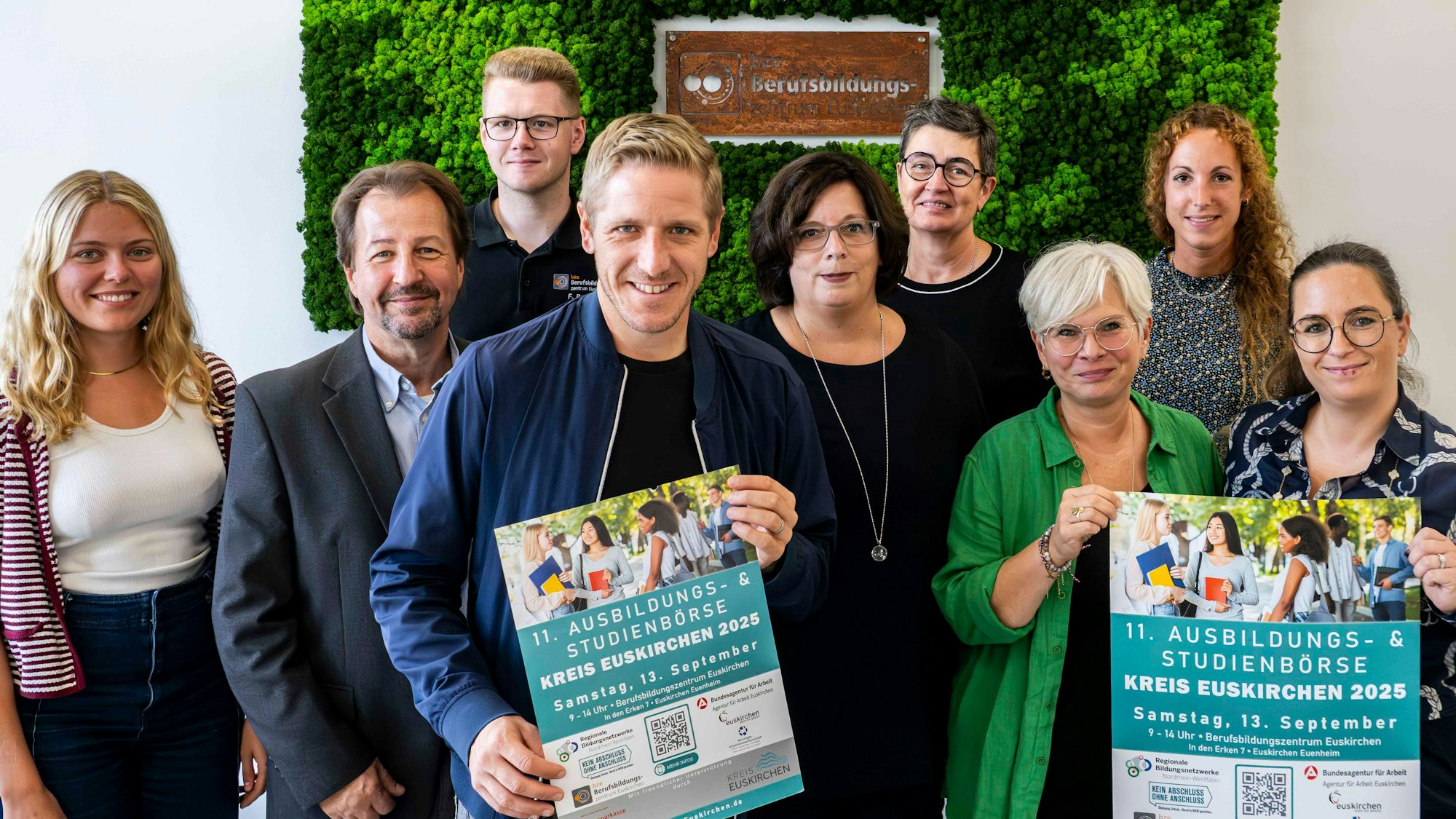 Sechs Frauen und drei Männer stehen in einer Gruppe zusammen. Einige halten das Veranstaltungsplakat vor sich.