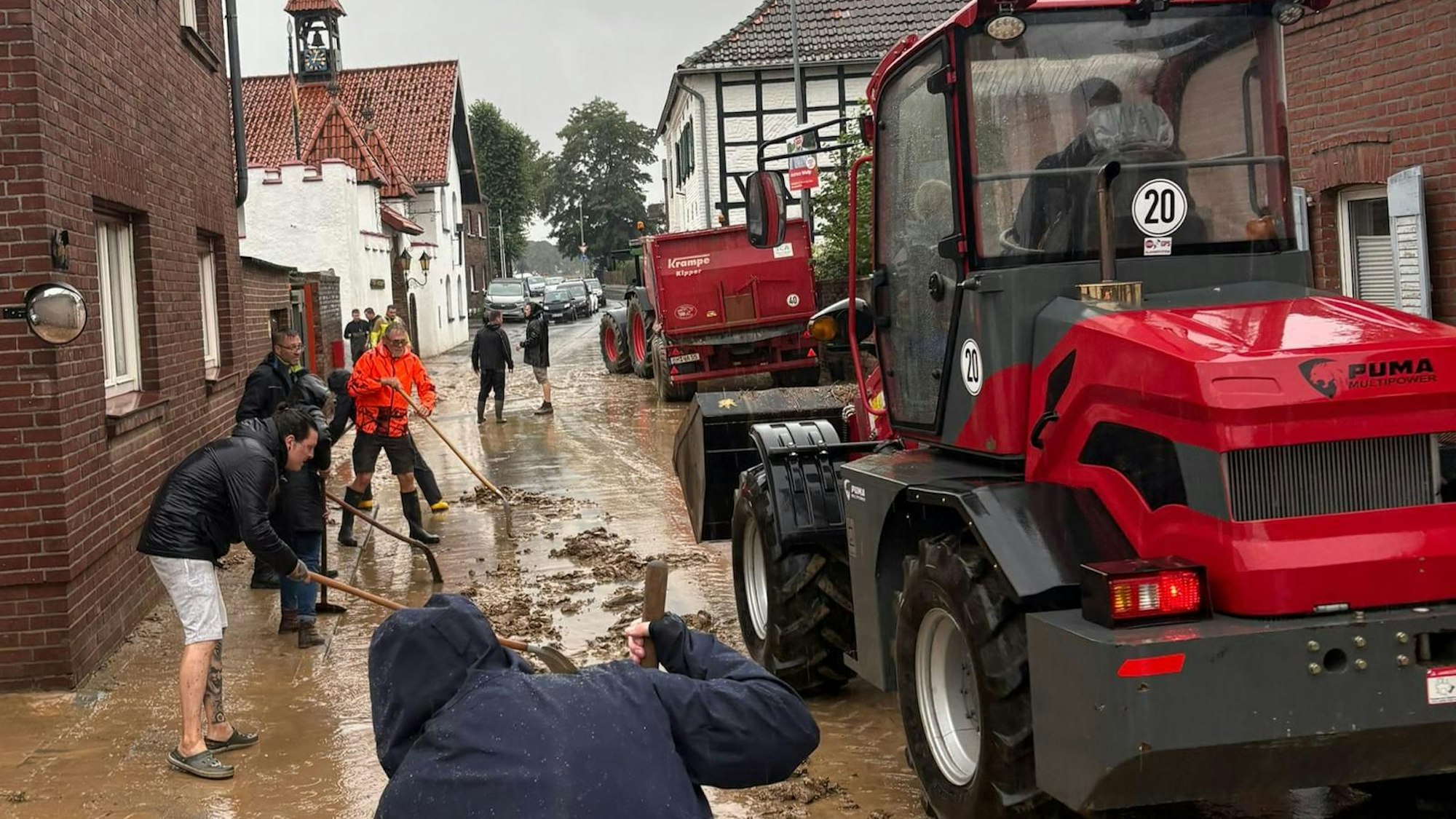Zu sehen sind Menschen, die Schlamm von einer Straße schaufeln.