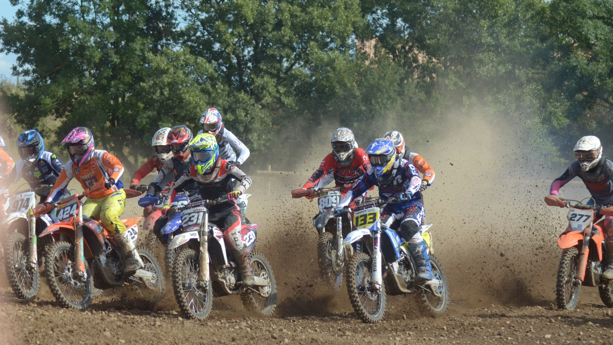 Die Motocrossfahrer ziehen eine Staubwolke hinter sich her.