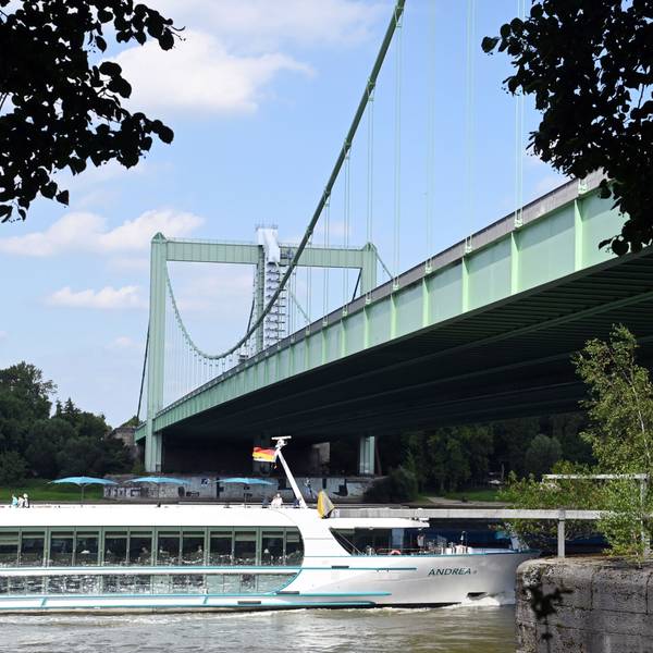 Ein Ausflugsschiff fährt unter einer grünen Hängebrücke her.
