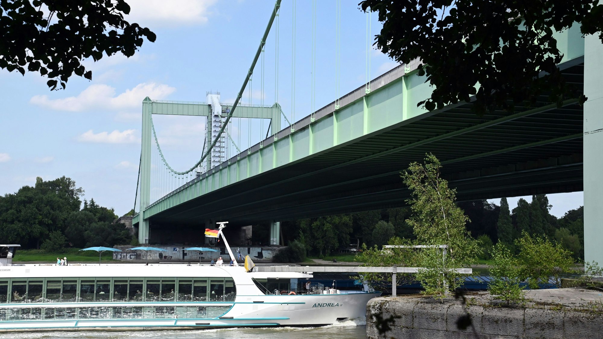 Ein Ausflugsschiff fährt unter einer grünen Hängebrücke her.