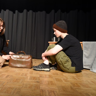 Zwei junge Leute sitzen auf dem Boden und sehen sich an.