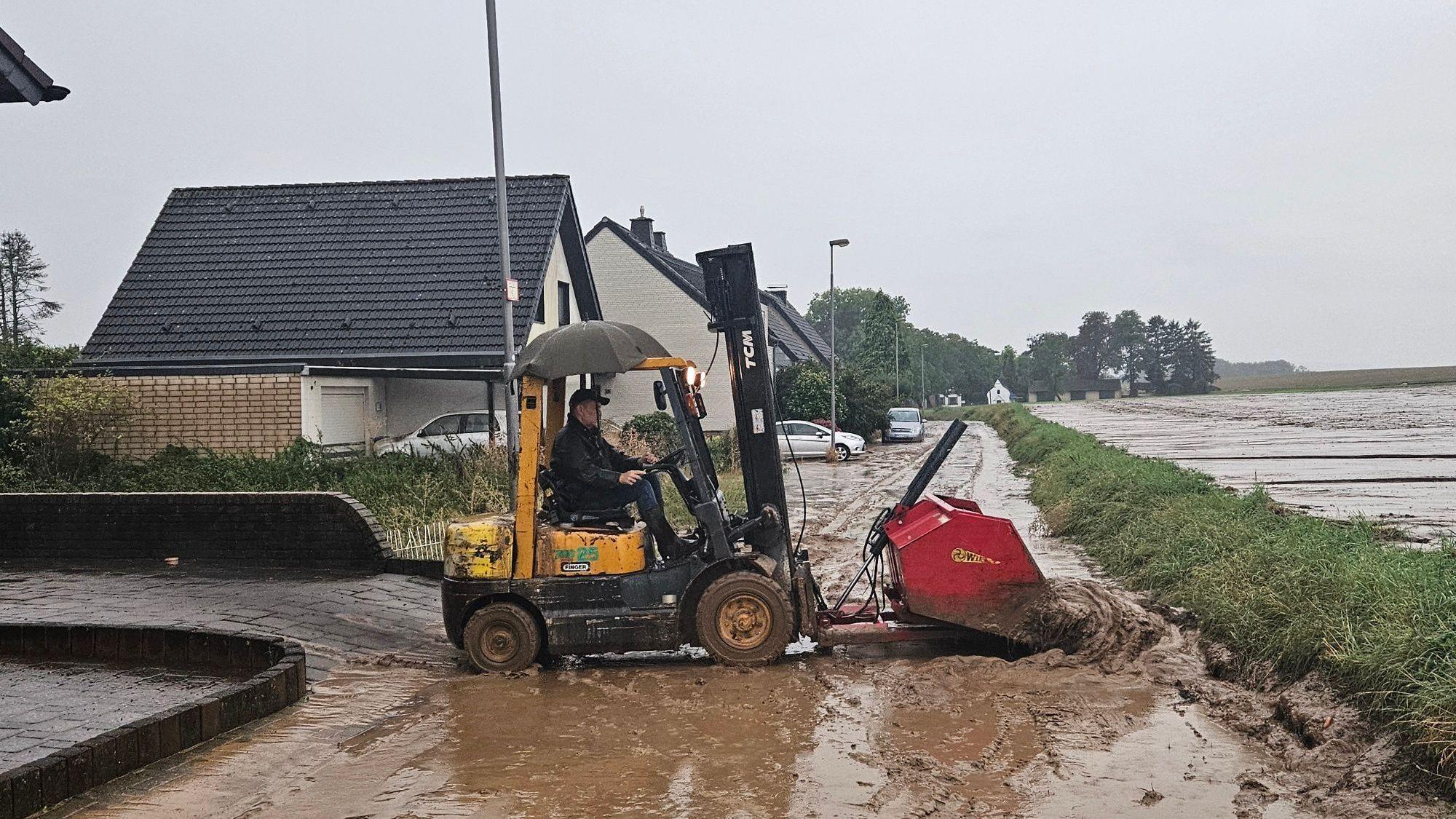 Zu sehen ist ein Mann, der mit einem Radlader Schlamm von einer Straße schiebt.