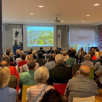 Zu sehen sind Menschen, die auf Stühlen sitzen und eine Präsentation verfolgen.