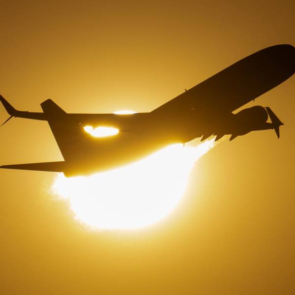 Ein Flugzeug fliegt an der untergehenden Sonne vorbei.