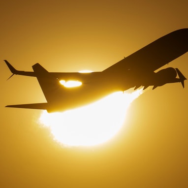 Ein Flugzeug fliegt an der untergehenden Sonne vorbei.