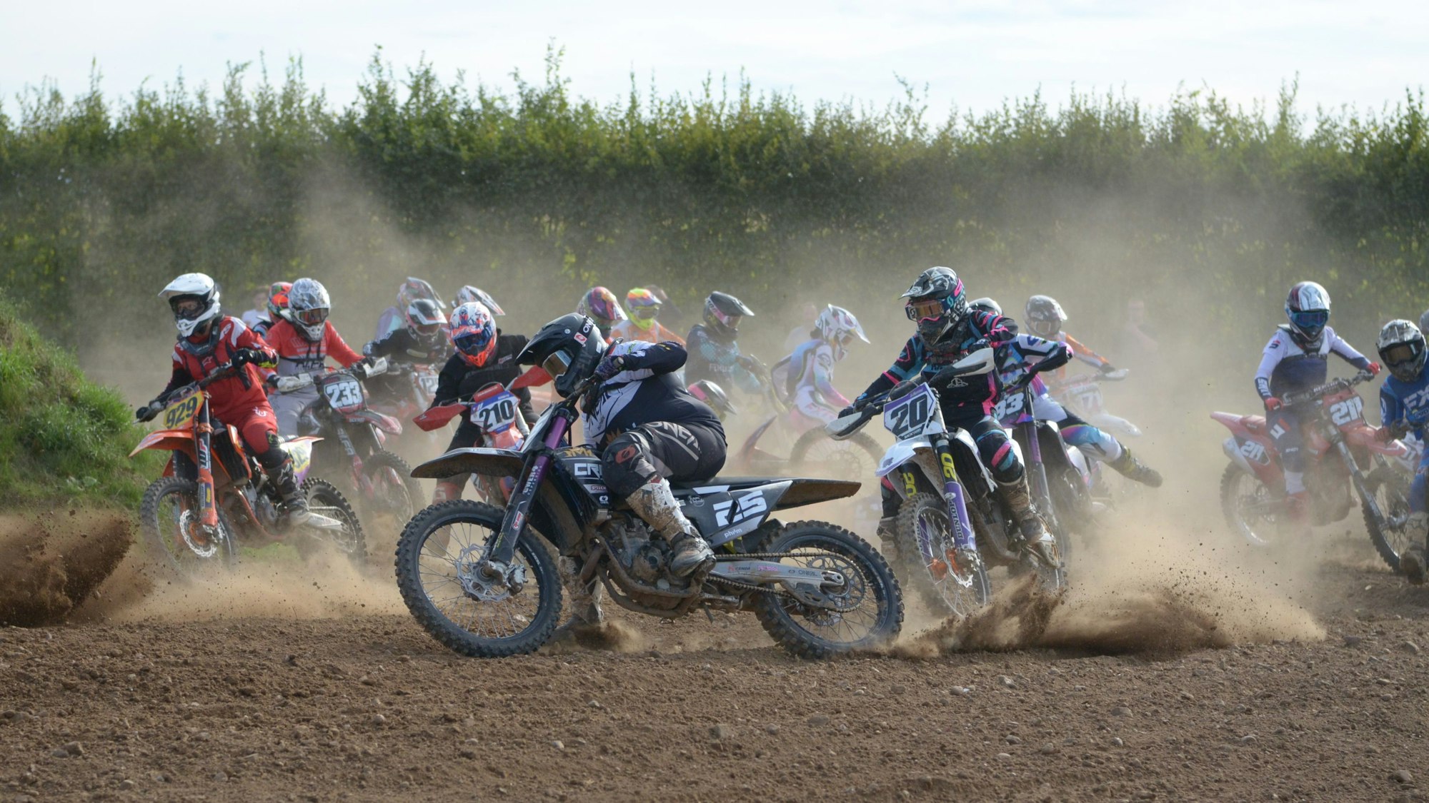 Mehr als ein Dutzend Motocrossfahrerinnen fahren auf einer staubigen Strecke durch eine enge Kurve.