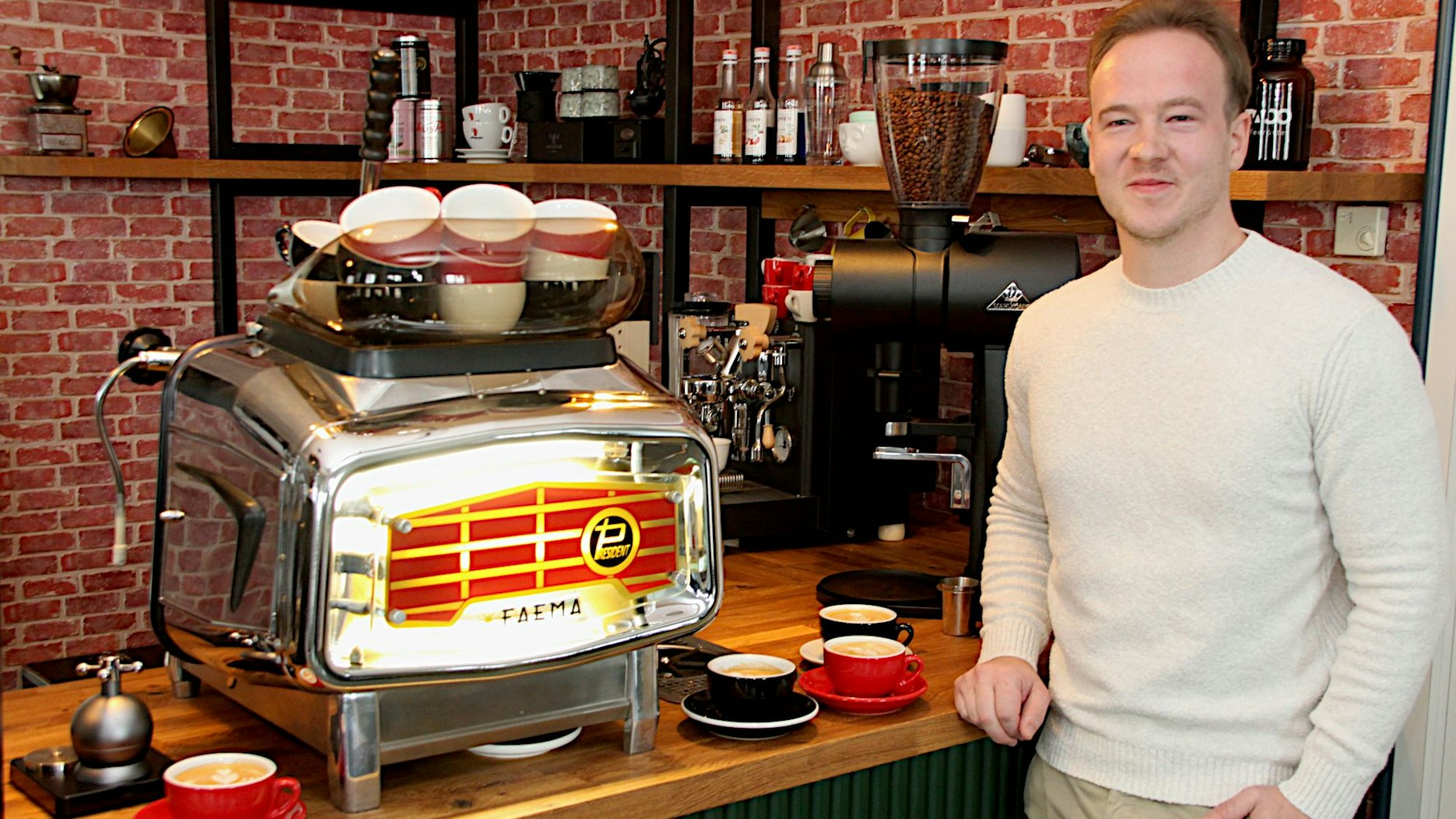 Anton Berg steht an der Holztheke seines Cafés. Dort steht eine verchromte Faema-Kaffeemaschine.