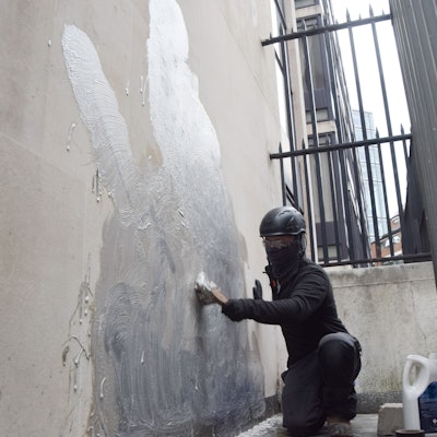 Eine Person schrubbt das neueste Kunstwerk des britischen Künstlers Banksy an den Royal Courts of Justice ab, das einen Richter zeigt, der einen Demonstranten mit einem Hammer schlägt.