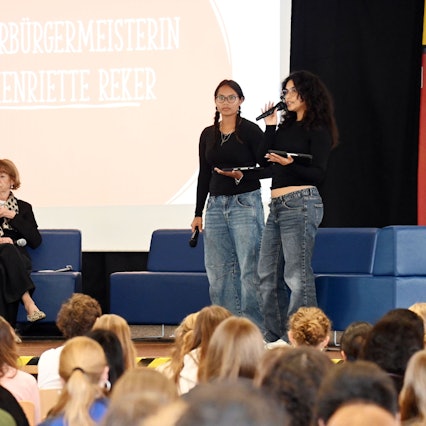 Die amtierende Oberbürgermeisterin Henriette Reker spricht mit Schülerinnen und Schülern der Oberstufe der Heinrich-Böll-Gesamtschule. Auf dem Podium: Schulleiter Rolf Grisard (v.l.), OB Henriette Reker und die Schülerinnen Luci Voisin und Leyla Celikaslan.