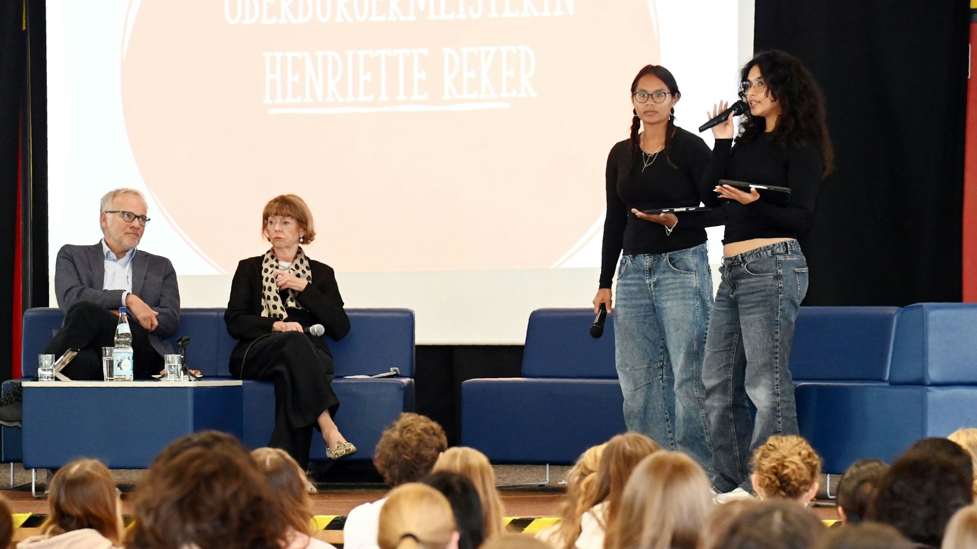 Die amtierende Oberbürgermeisterin Henriette Reker spricht mit Schülerinnen und Schülern der Oberstufe der Heinrich-Böll-Gesamtschule. Auf dem Podium: Schulleiter Rolf Grisard (v.l.), OB Henriette Reker und die Schülerinnen Luci Voisin und Leyla Celikaslan.