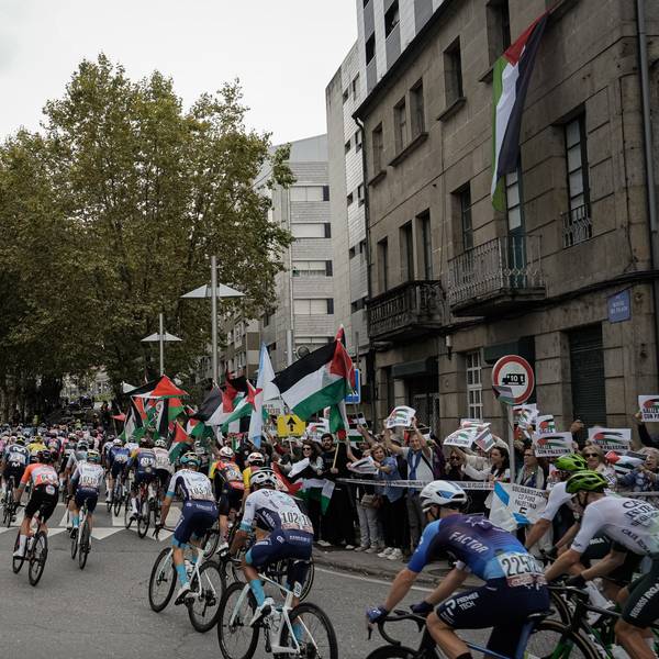Menschen protestieren mit palästinensischen Fahnen gegen den Gaza-Krieg, als Teilnehmer der Vuelta a España in ein Stadt fahren.