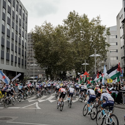 Menschen protestieren mit palästinensischen Fahnen gegen den Gaza-Krieg, als Teilnehmer der Vuelta a España in ein Stadt fahren.