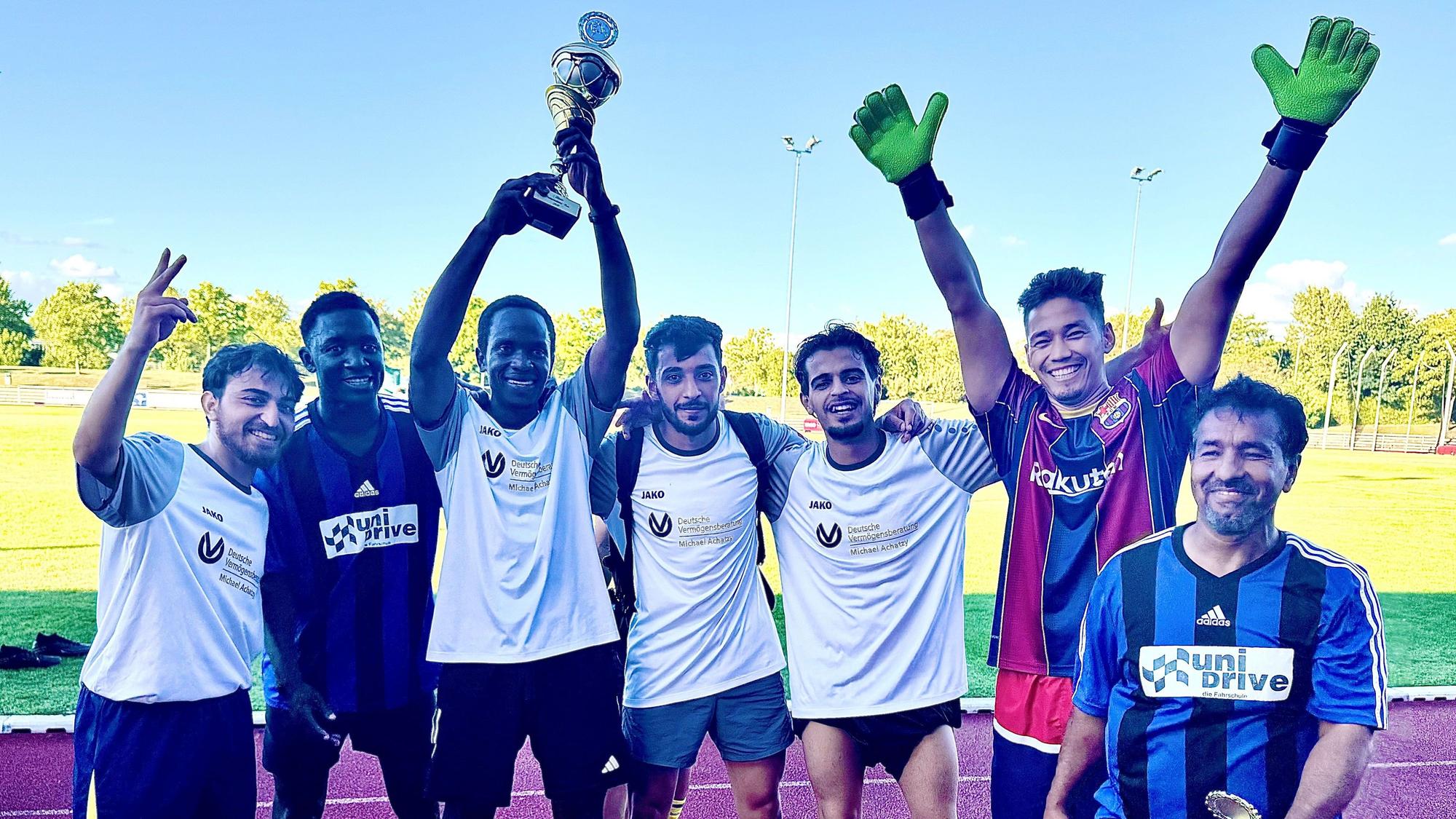 Die Mitglieder der siegreichen Mannschaft stehen jubelnd nebeneinander, einer hält einen Pokal in die Höhe.