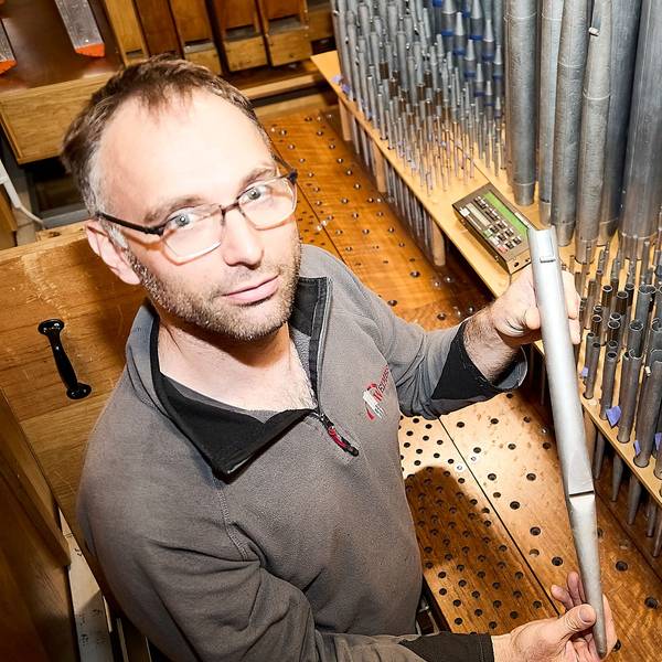 Markus Moutschen hält eine Orgelpfeife in den Händen, dahinter sind zahlreiche Pfeifen zu sehen.