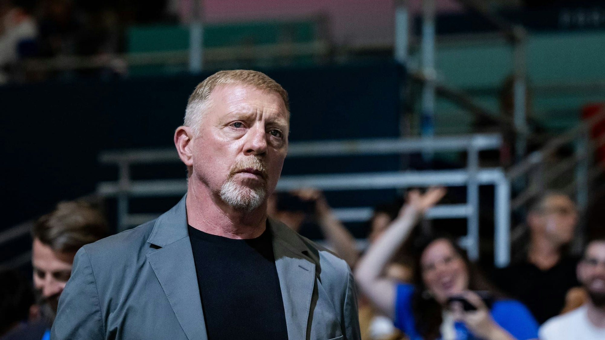 Boris Becker, im grauen Anzug, schaut einem Handballspiel zu.