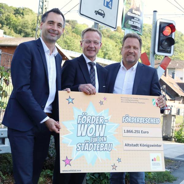 Drei Männer halten ein großes Schild mit der Aufschrift „Förder-Wow ... für den Städtebau“.