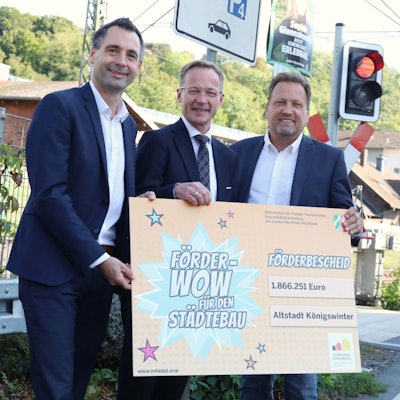 Drei Männer halten ein großes Schild mit der Aufschrift „Förder-Wow ... für den Städtebau“.