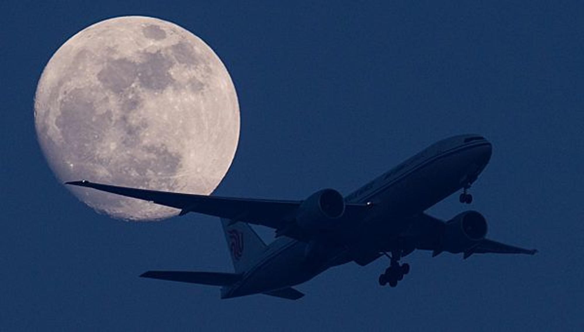 Ein Flugzeug fliegt bei Nacht vor dem Mond