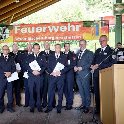 Die geehrten Feuerwehrleute haben sich vor einer Feuerwehr-Fahne zum Gruppenbild zusammengestellt.